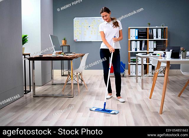 Full Length Of Female Janitor Mopping Floor In Office