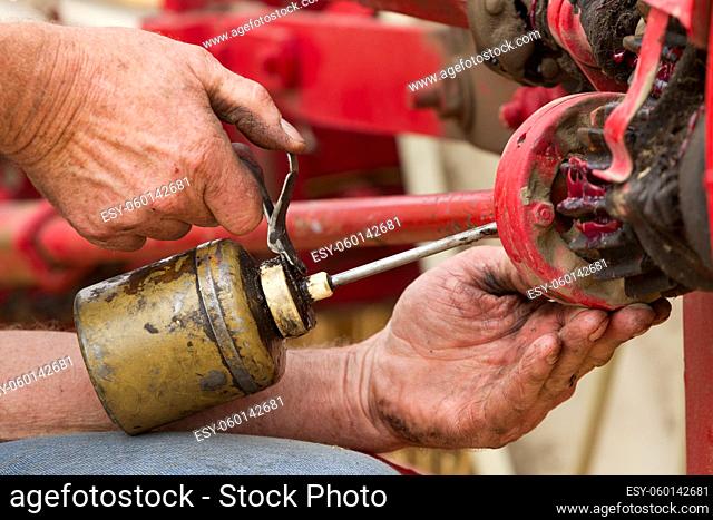 The hands of a man using an old oil can to grease the machinery