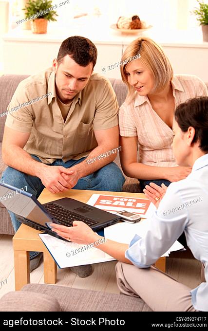 Young couple listening to estate agent showing new house on laptop