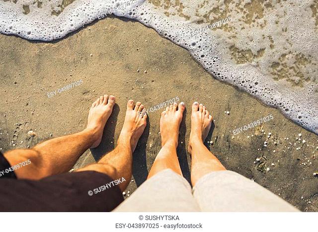 Legs of young couple standing on the the sand with ocean near by