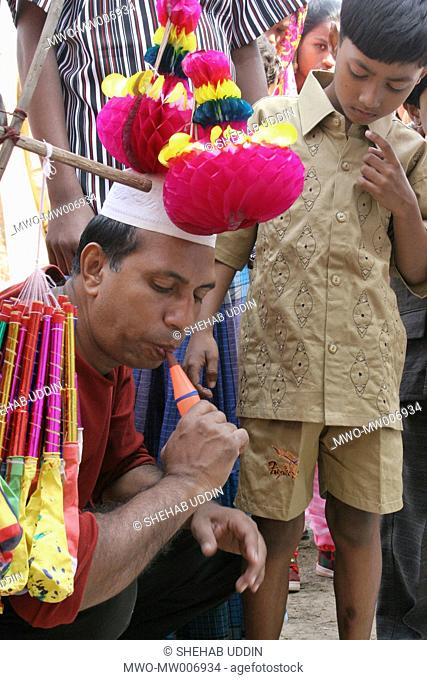 A Muslim father tests a balloon flute toy for his son at a village fair during the Eid-ul-Adha festival Mayshaghuni, Rupsha, Khulna, Bangladesh January 01