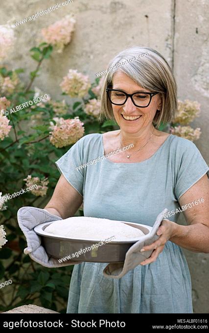 Excited woman carrying baked bread pan at back yard