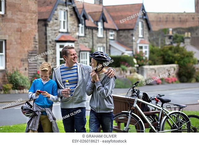 Father and Sons stopping in a village in the middle of their bike ride to take a drink. They are wearing casual clothing and smiling