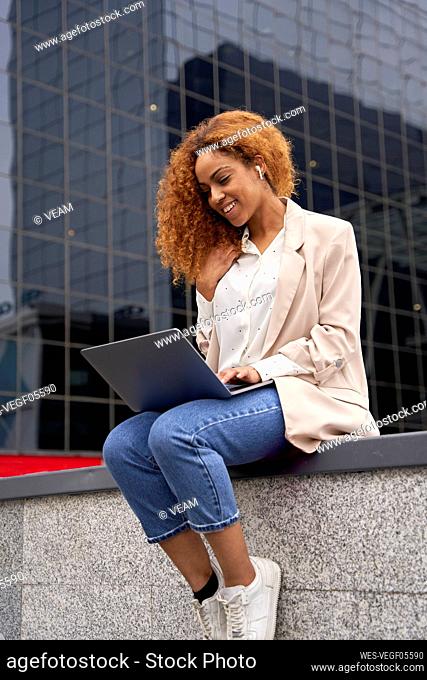Young businesswoman working on laptop outside office building