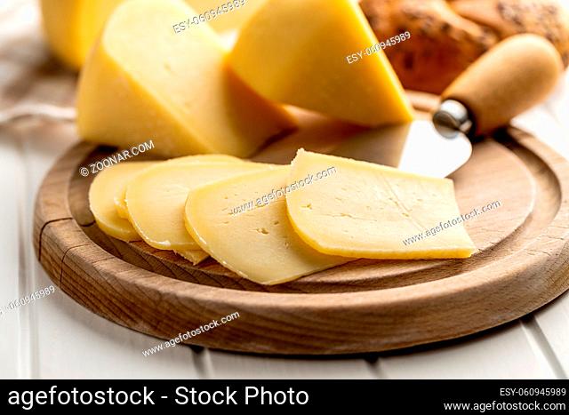 Block of hard cheese. Sliced cheese on cutting board