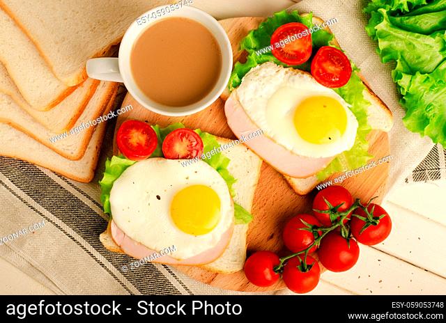 Ham sandwich with scrambled egg, tomato, lettuce, delicious healthy breakfast and coffee on white wooden background