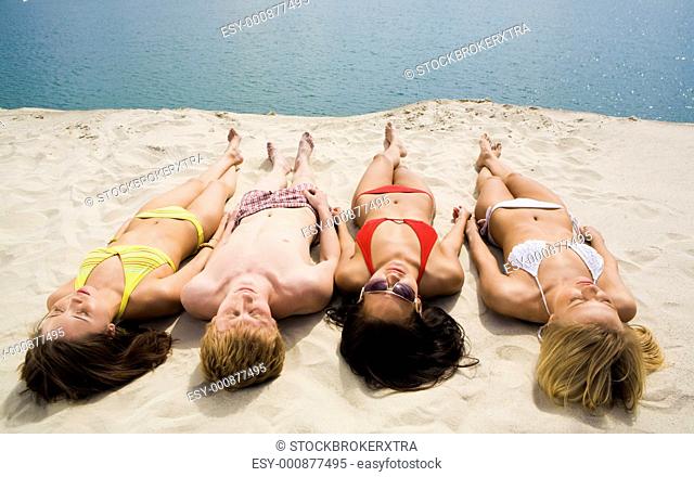 Photo of several girls and a guy sunbathing on sandy beach by the lake