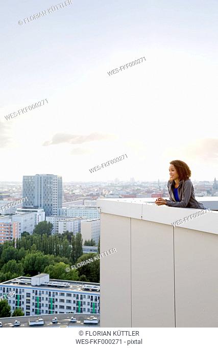 Germany, Berlin, Young woman on rooftop terrace, looking at view