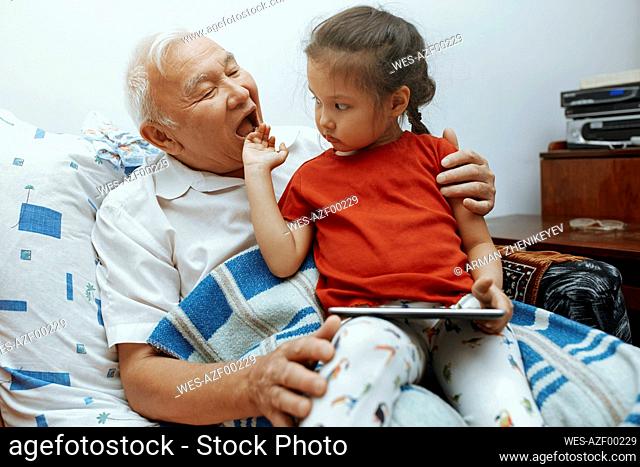 Girl sitting on grandfather's lap with digital tablet at home