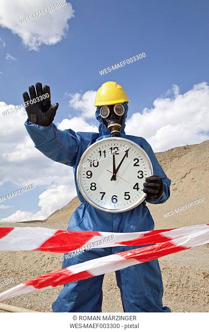 Germany, Bavaria, Man in protective wear with clock near sand dune and cordon tape in foreground