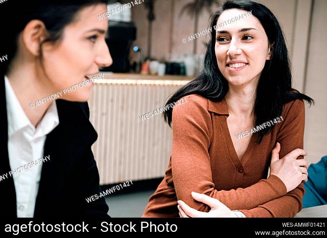 Smiling businesswoman discussing with office friend at cafe