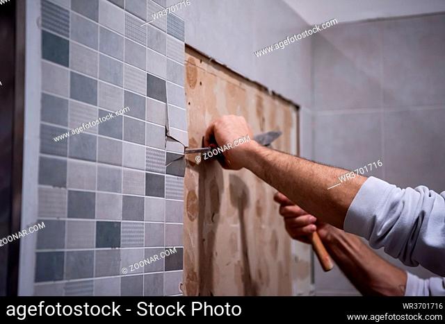 professional worker remove demolish old tiles in a bathroom with hammer and chisel