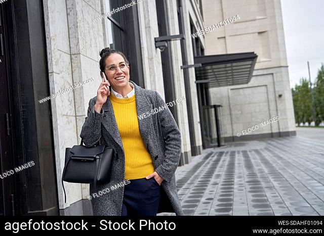 Smiling businesswoman talking on mobile phone while walking in city