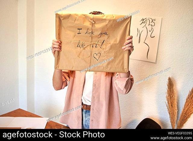 Female freelancer showing wrapped delivering package against wall at home