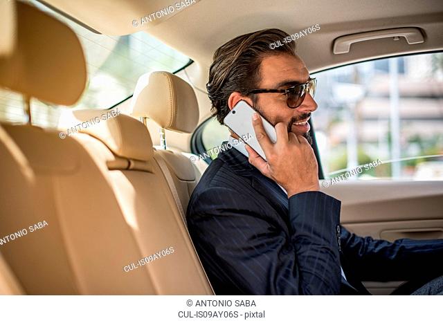 Young businessman in car backseat wearing sunglasses and talking on smartphone, Dubai, United Arab Emirates