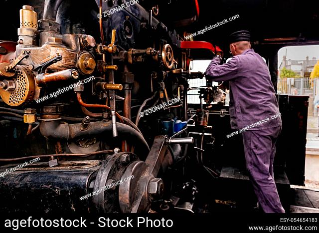 Selective focus on steam engine elements or parts in steam train cabin with unrecognisable engineer or train driver working on cranks, Ireland