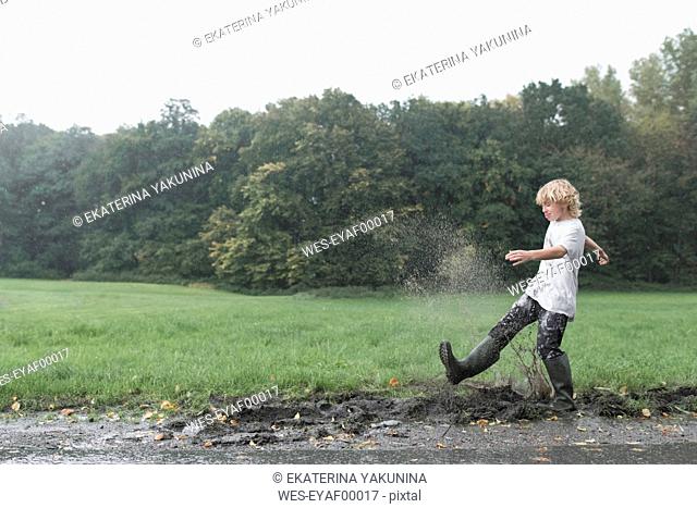 Boy splashing with dirty water of puddle
