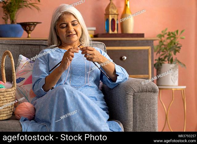 Old woman knitting while sitting on sofa in living room