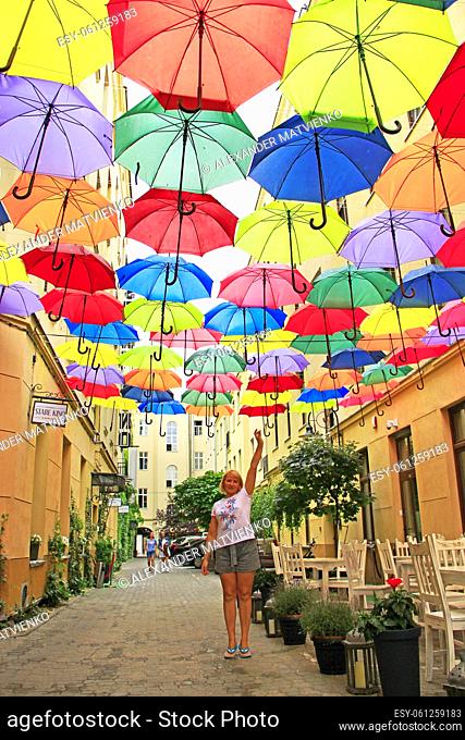 Street decoration. woman standing under colored umbrellas hanging at top. Set of different umbrellas. Local landmark. Cafe decoration in Lodz