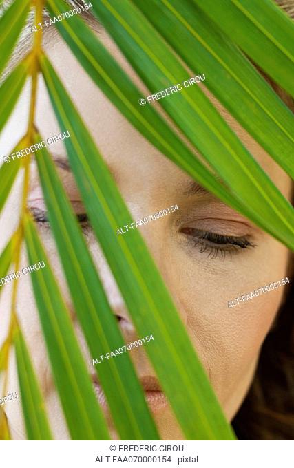 Woman behind palm leaf, portrait