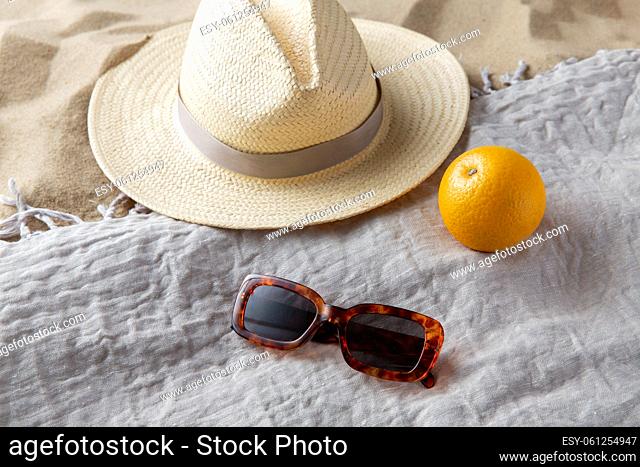 straw hat, sunglasses and orange on beach blanket