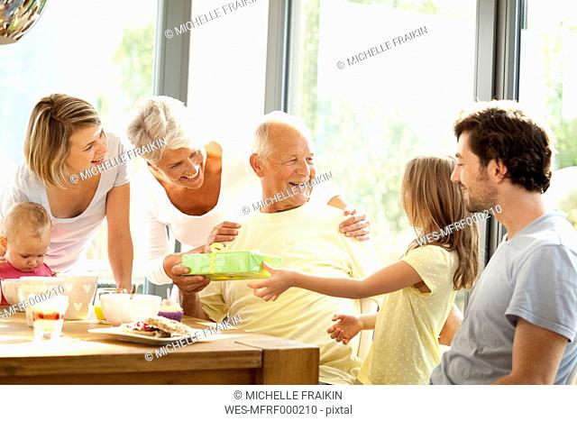 Senior man receiving present from his granddaughter at breakfast table