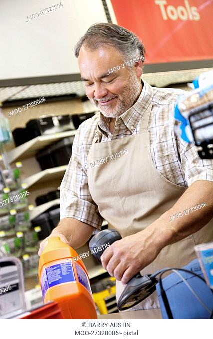 Happy mature salesperson using barcode reader at checkout counter in hardware counter