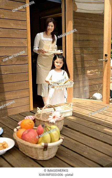 A small girl helping her mother to place meal on the wooden table