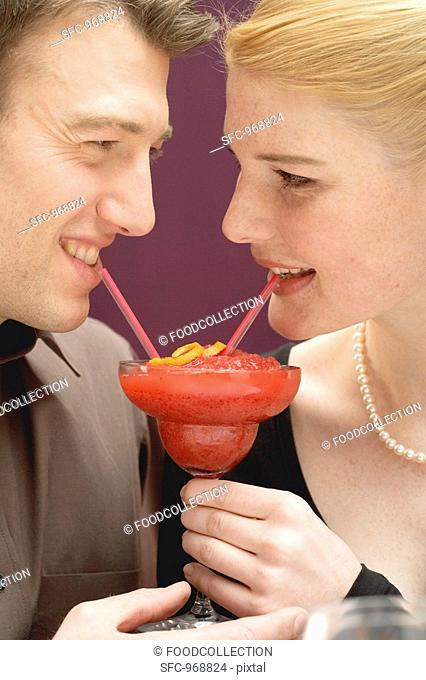 Romantic couple drinking Strawberry Daiquiri out of one glass
