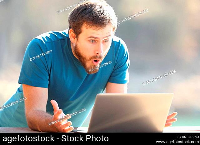 Amazed man checking laptop content outdoors a sunny day
