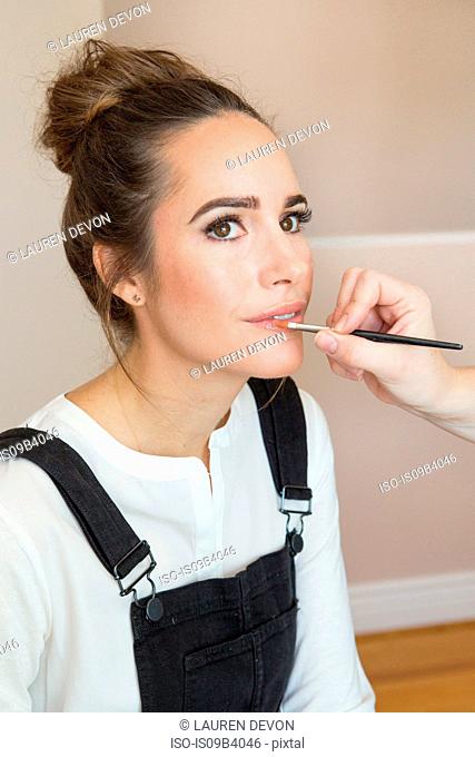 Hand of make up artist applying lip gloss to female fashion and lifestyle blogger