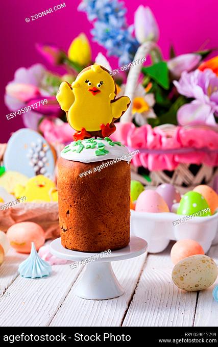 Close-up small traditional Easter breads, glazed and decorated for children with ginger breads in chicken shape. Basket with bright colorful flowers on...