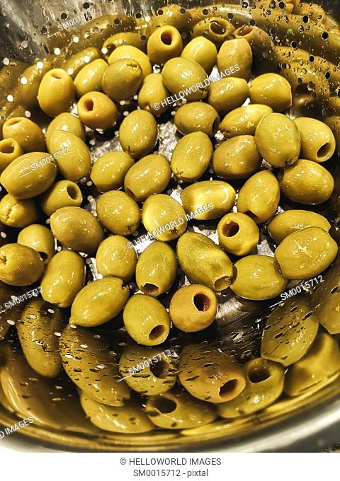 Green olives in colander with reflection
