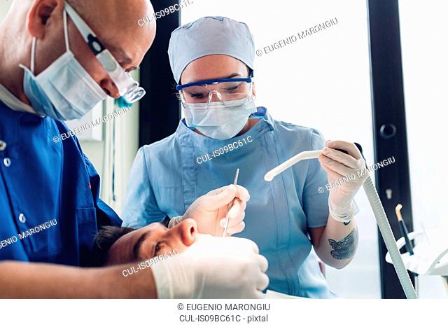 Dentist and dental nurse carrying out dental procedure on male patient, close-up