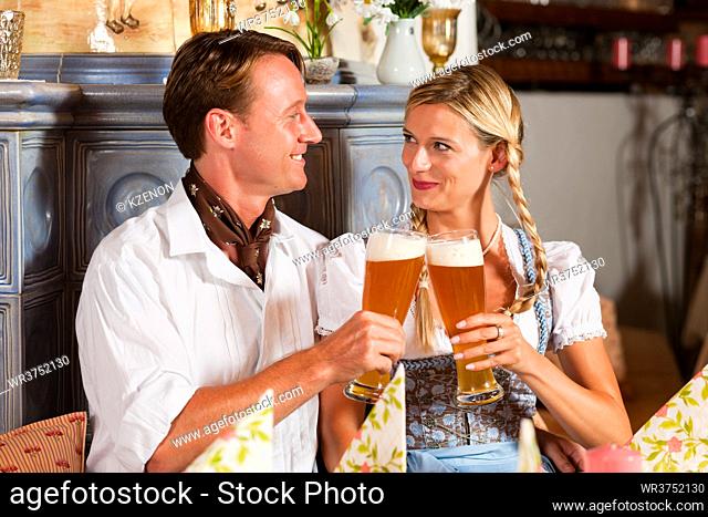 Couple in Bavarian Tracht drinking wheat beer in a typical pub, clinking glasses