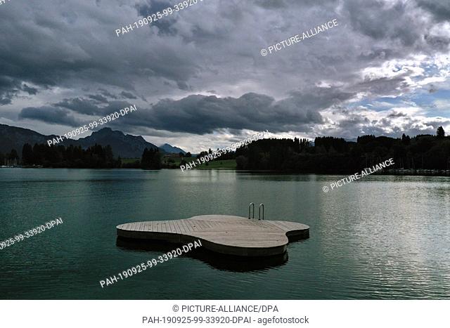 25 September 2019, Bavaria: Under dense clouds a deserted bathing platform floats on the Forggensee (aerial photograph with a drone)