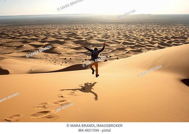 Young man walking down a sand dune, dune landscape Erg Chebbi, Merzouga, Sahara, Morocco