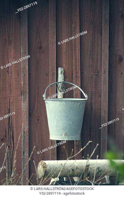 Old bucket hanging on wall of rural building. Vintage farm equipment