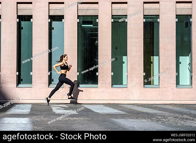 Young woman jogging on footpath by building