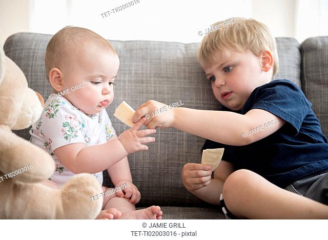 Brother (2-3) sharing crackers with baby sister (12-17 months)