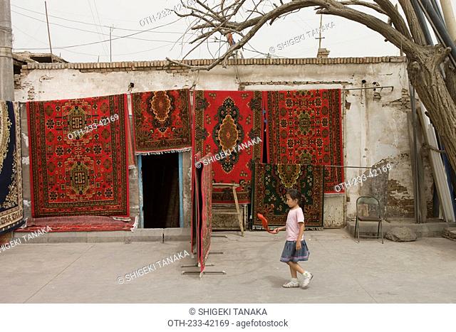 An Uyghur gir walks passing by a carpet shop, Old town of Kashgar, Xinjiang Uyghur autonomy district, Silkroad, China
