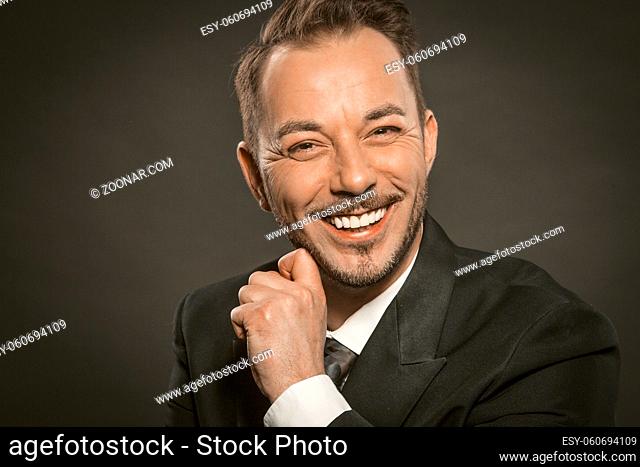 Cheerful businessman smiles broadly touching his beard and looking at camera. Close up portrait of Caucasian handsome man in formalwear. Toned image