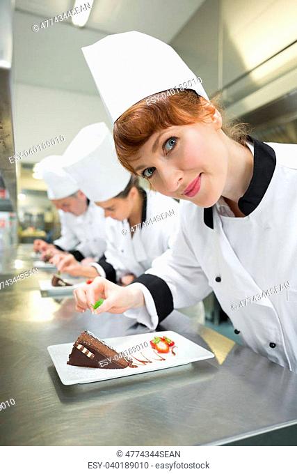 Happy chef garnishing dessert plate standing in a kitchen