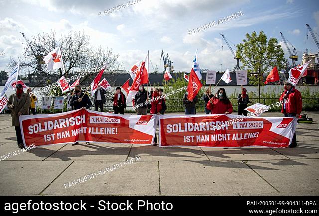 01 May 2020, Hamburg: Participants in a demonstration on the nationwide ""Labour Day"" stand with banners saying ""Solidarisch ist man nicht allein"" (""One is...