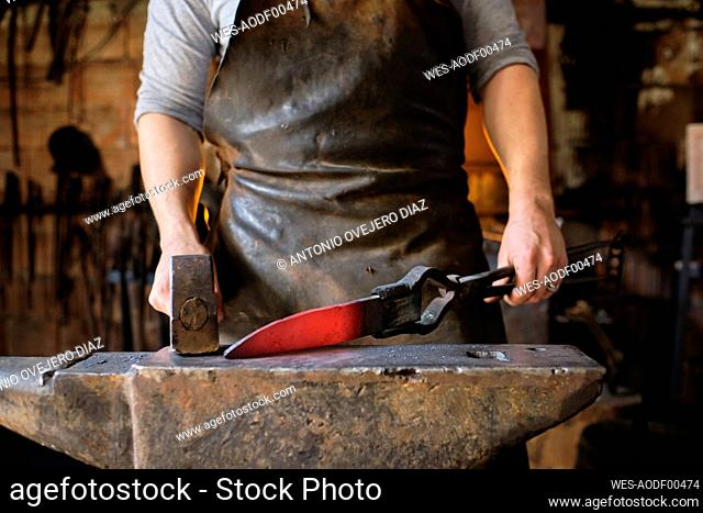 Blacksmith making knife of metal on anvil at blacksmith shop