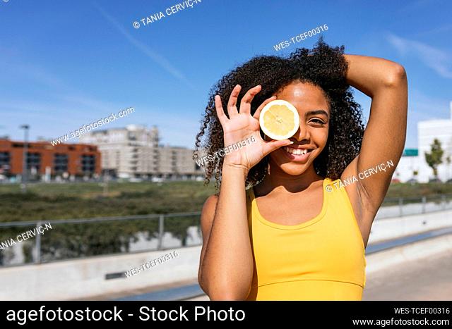 Portrait of laughing young woman covering eye with lemon half