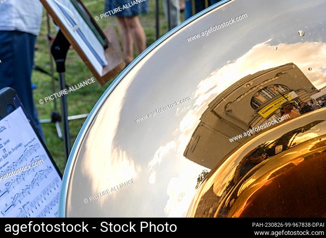 26 August 2023, Brandenburg, Cottbus: A ""Theater-Stadt-Fest"" poster attached to the Cottbus State Theater's Great House is reflected in a trombone at a...