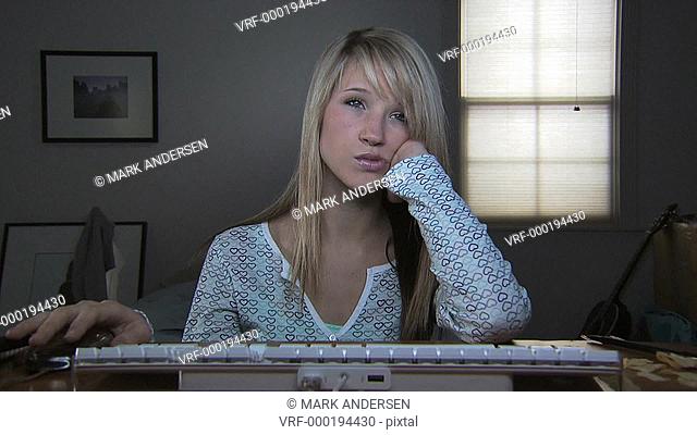 A young woman at a keyboard looking bored