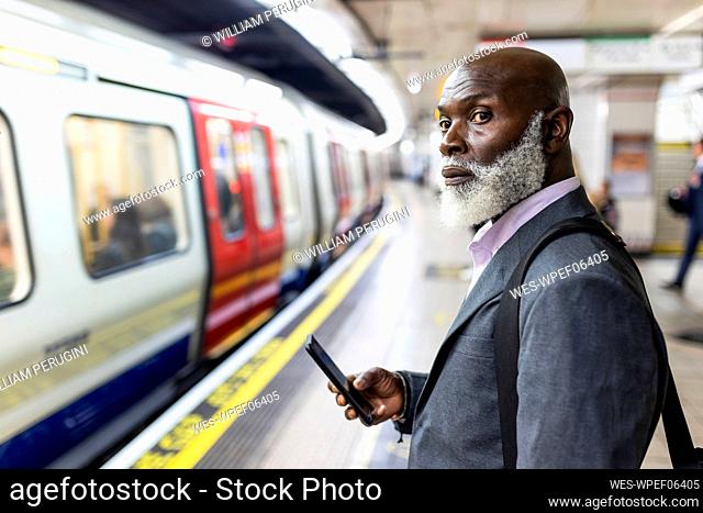 Senior passenger with mobile phone looking at subway train