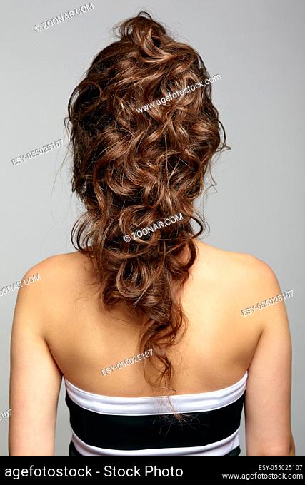 Back view portrait of beautiful young dark brunette woman. Female with creative hairdo on gray background